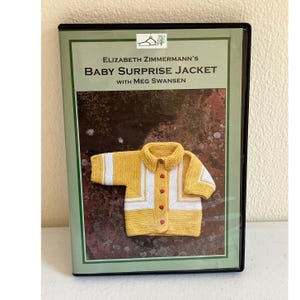 May include: A DVD case featuring Elizabeth Zimmermann's Baby Surprise Jacket with Meg Swansen. The cover displays a yellow and white knitted baby jacket with red buttons against a textured background. The text includes the title and author names.
