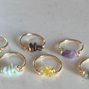Peut inclure: Six bagues en or avec des pierres précieuses de différentes couleurs. Les bagues sont faites avec du fil enroulé autour des pierres. Les pierres sont turquoise, noires, améthyste, vertes, jaunes et blanches.