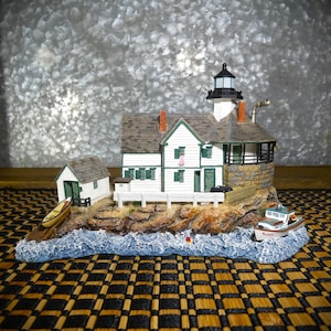 May include: A detailed miniature lighthouse scene. The white and green lighthouse has a black lantern room and is connected to a house. A small boat and a boathouse are also included. The base is designed to look like a rocky shore with waves.