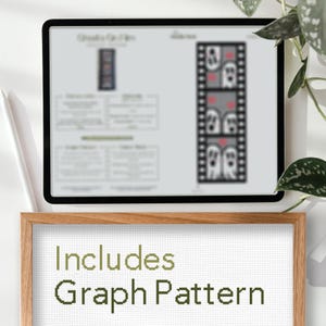 May include: A digital screen displaying a cross-stitch pattern of a film strip with three ghosts. The screen is on a wooden table with a framed piece of white fabric that says "Includes Graph Pattern".