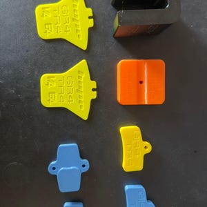 May include: A collection of brightly coloured plastic bicycle components, including yellow, orange, blue, and black pieces. Some parts are printed with the text "GR4 TR4 14 E4". The parts are arranged on a dark surface.