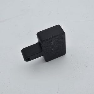 May include: A black, textured, rectangular object with a small, cylindrical extension. The object is set against a white background. The item appears to be a small tool or component, possibly for a larger device.