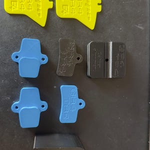 Peut inclure: Un assortiment de plaquettes de frein de vélo de différentes couleurs. Les plaquettes comprennent du jaune, du bleu, du noir et un composant noir en forme de U. Les plaquettes jaunes portent l'inscription "GR4" et "hope".