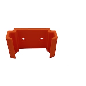 May include: An orange plastic bracket with two circular holes and a U-shaped opening. The bracket has a rectangular top and two side supports, designed to hold an item. The item is likely for tools or equipment.