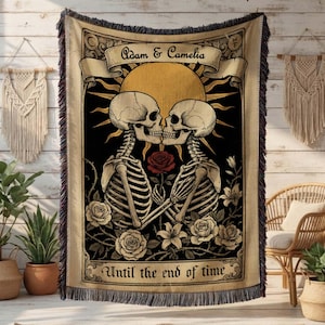 May include: A woven throw blanket featuring a romantic gothic design. Two skeletons are kissing in front of a sun, holding a rose. The words "Adam & Camelia" and "Until the end of time" are displayed on the blanket. The blanket has a fringed edge.