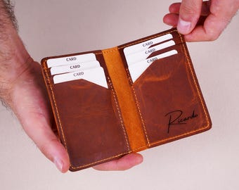 May include: Open brown leather wallet with multiple card slots, holding several white cards labeled "CARD." The wallet has a contrasting tan interior and the name "Ricardo" is written in cursive on the front.