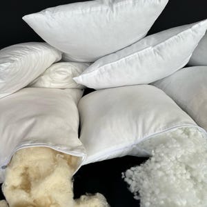 May include: A stack of white pillowcases with zippers open, revealing the white and cream-colored filling inside.