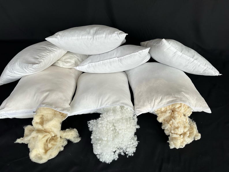 May include: Eight white pillowcases with zippers, some are open to reveal the white and cream-colored filling inside.