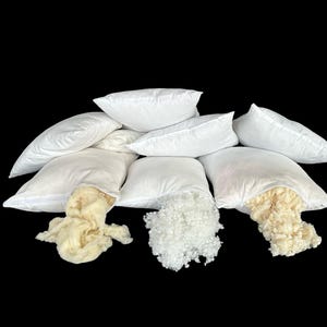 May include: A group of eight white pillowcases with different types of filling. The pillowcases are arranged in a pyramid shape with the filling spilling out of the bottom of the pillowcases. The fillings include white polyester fiberfill, white down feathers, and cream-colored wool.