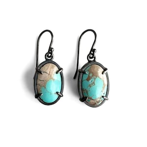 May include: A pair of oval turquoise earrings with a silver-tone metal frame and hook. The turquoise stones have a mottled pattern of blue and brown. The earrings are displayed against a white background.