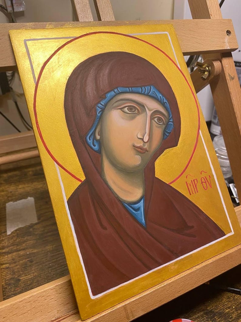 May include: A hand-painted icon depicting a woman with a blue head covering and a red robe. The icon is set against a gold background with a red halo. The text "HIP EV" is written in the lower right corner.