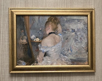 May include: A framed painting with a gold ornate frame. The artwork depicts a woman in a white dress, seated and facing away from the viewer. The painting has a soft, impressionistic style with muted blues, whites, and golds.
