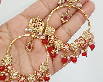 May include: Gold-tone hoop earrings featuring a circular top stud with a floral design, accented with small white pearls and red stones. The large hoops are decorated with floral motifs, dangling red beads, and white pearl accents throughout.