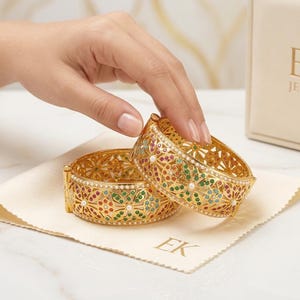 Puede incluir: Dos brazaletes de oro con intrincados patrones de filigrana, incrustados con pequeñas piedras preciosas redondas rojas, verdes y azules, y acentuados con diminutas perlas blancas. Se presentan con un paño de marca y una caja con la etiqueta EK JEWELS.