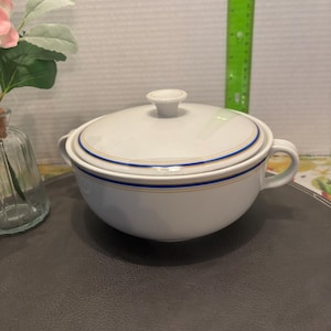 Peut inclure: Bol en céramique blanche avec un couvercle. Le bol est orné d'une bordure bleue et dorée.