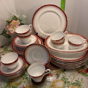May include: A set of red and gold rimmed china teacups and saucers. The set includes a large dinner plate and several smaller plates.