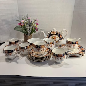 May include: A classic tea set featuring a navy blue and gold floral pattern. The set comprises a teapot, cups, saucers, and a creamer. The cups and saucers are arranged, and the teapot is the focal point of the image.