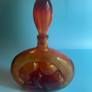May include: A vintage amber glass decanter with a unique, abstract design. The decanter has a rounded body with a bulbous, pointed stopper.