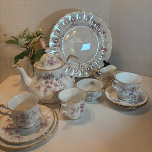 May include: A floral patterned tea set, including a teapot, cups, saucers, a sugar bowl, and a serving plate. The edges are trimmed with gold. The floral design features pink roses and green leaves.