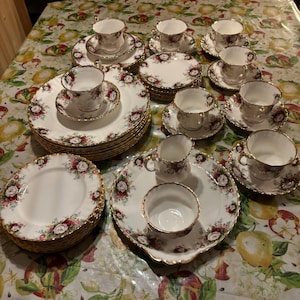 May include: A vintage floral china tea set with gold trim. The set includes a variety of sizes and shapes, including teacups, saucers, dessert plates, and dinner plates.