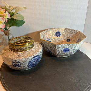 May include: A pair of vintage ceramic bowls with a gold rim and intricate blue and white floral patterns. The bowls are on a grey round placemat.