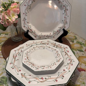Könnte beinhalten: Weißes achteckiges Geschirrset mit rosa Schleifen- und Blumendesign. Die Teller haben einen grünen Rand und einen gepunkteten Rand. Das Set enthält große und kleine Teller, ideal für ein formelles Esszimmer.