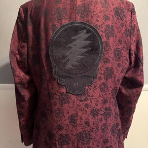 May include: A burgundy blazer with a black floral pattern. A black skull and lightning bolt patch is on the back.