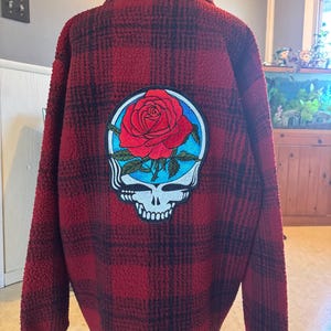 May include: Red and black plaid flannel shirt with a large embroidered patch of a rose and a skull on the back.