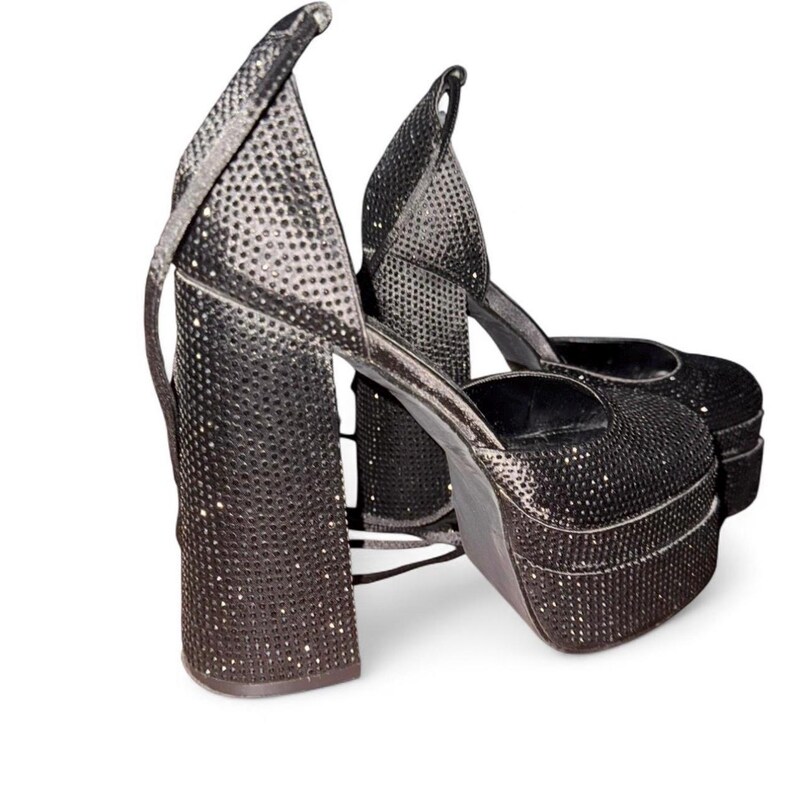 K&ouml;nnte beinhalten: Ein Paar schwarze Plateau-High Heels, bedeckt mit kleinen, funkelnden Verzierungen. Die Abs&auml;tze haben dicke Blockabs&auml;tze und Kn&ouml;chelriemen. Die Schuhe haben eine runde Spitze und eine hohe Plateausohle.