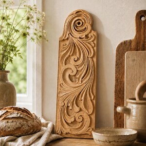 May include: A rectangular light brown wooden panel featuring an intricate, raised relief carving of swirling acanthus leaf patterns. The carving is symmetrical and ornate, with a rounded top edge, showcasing natural wood grain and texture.