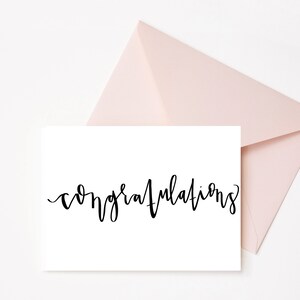 May include: A white card with the word "congratulations" written in black cursive script. The card is sitting on top of a light pink envelope.