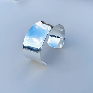 May include: A silver cuff bracelet with a smooth, polished finish. The bracelet is open and has a slightly curved shape.