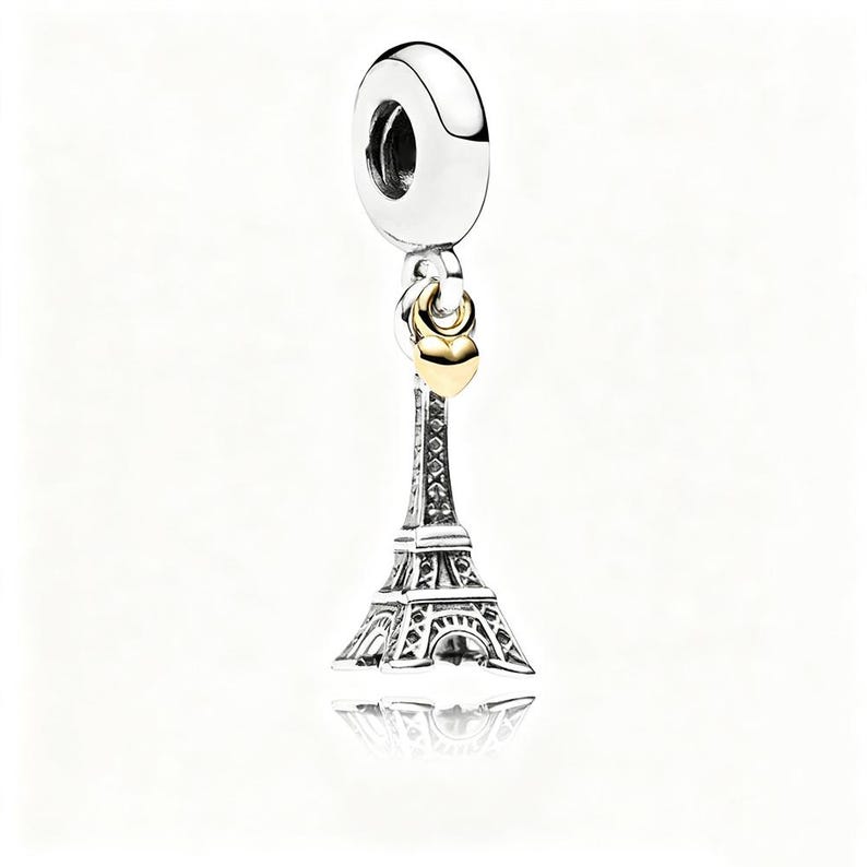 May include: A silver charm with a gold heart and a detailed Eiffel Tower design. The charm has a silver loop at the top for attachment. The Eiffel Tower charm is a popular travel souvenir.