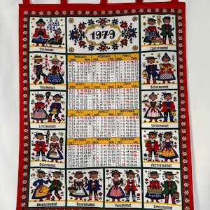 May include: A red fabric wall calendar for 1979, featuring folk art illustrations for each month. Each month has a different illustration of people in traditional clothing. The calendar has a red border.
