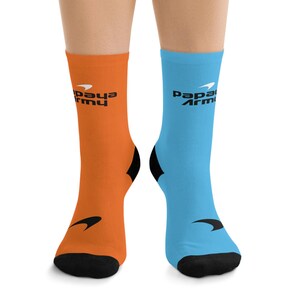May include: A pair of crew socks, one orange and one light blue, each with a black heel and toe. The orange sock has the text "Papaya Army" in black, and the light blue sock has the same text. A black arrow design is on each sock.