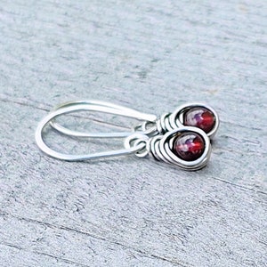 May include: A pair of silver dangle earrings with red gemstone beads. The earrings are made with wire wrapped around the beads.