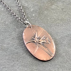 May include: A copper pendant necklace with a detailed floral design. The pendant is oval shaped and has a hammered texture. The chain is silver.