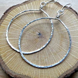 May include: A pair of silver hoop earrings with a hammered texture. The earrings are large and circular, and they have a simple, elegant design.
