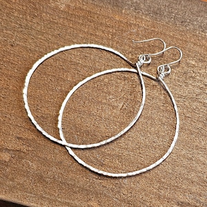 May include: A pair of silver hoop earrings with a hammered texture. The hoops are large and have a simple, elegant design.