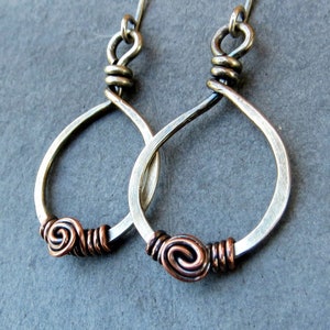 May include: A pair of silver and copper earrings with a twisted wire design and a spiral accent. The earrings are handmade and have a rustic, bohemian style.