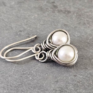 May include: A pair of silver wire wrapped earrings with white pearl accents. The earrings have a simple hook closure.