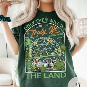 May include: Green t-shirt with a graphic of Mickey Mouse and friends riding a boat in a green dome with the text "Only then will we truly be living with the land".