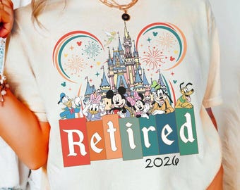 May include: Cream-colored t-shirt featuring a colorful graphic of Disney characters, a castle, fireworks, and the word "Retired" with the year "2026". The design includes Mickey and Minnie Mouse, Donald and Daisy Duck, Goofy, and Pluto.