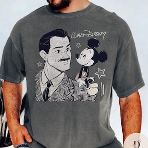 May include: Gray t-shirt featuring a black and white illustration of Walt Disney with Mickey Mouse. The text "Walt Disney" is written above the characters. The shirt has a vintage, distressed look.
