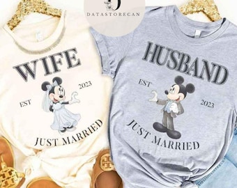 Könnte beinhalten: Zwei T-Shirts mit einem Mickey Mouse und Minnie Mouse Design. Das weiße T-Shirt sagt "Wife Est. 2023 Just Married" und das graue T-Shirt sagt "Husband Est. 2023 Just Married".