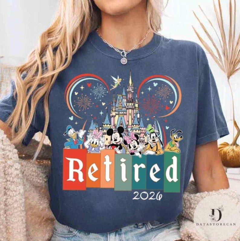 May include: Navy blue t-shirt featuring a colorful graphic of Disney characters, a castle, fireworks, and the word "Retired" in large white letters. The year "2026" is printed below the word "Retired".