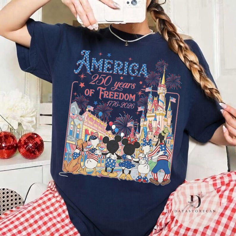 May include: Navy blue t-shirt with the text "America 250 years of Freedom 1776-2026". The graphic features a patriotic design with fireworks, a castle, and cartoon characters. The shirt is a celebration of American history.