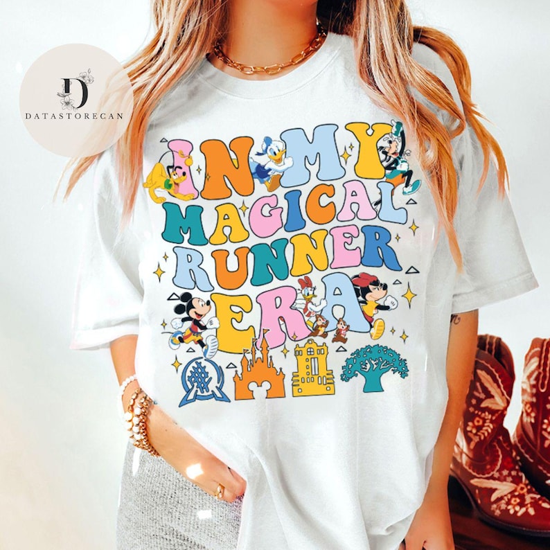 K&ouml;nnte beinhalten: Wei&szlig;es T-Shirt mit einem bunten Grafikdruck, der "In My Magical Runner Era" lautet. Die Grafik enth&auml;lt Mickey Mouse, Donald Duck und andere Disney-Figuren.