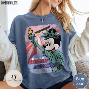 May include: Blue jean Comfort Colors t-shirt with a graphic of Mickey Mouse as the Statue of Liberty, holding a torch. The design includes an eagle, American flag, and the text "1776-2026 Soarin' Across America 250 years of freedom."
