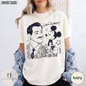 May include: Ivory-colored t-shirt featuring a black and white illustration of Walt Disney and Mickey Mouse. The text "Walt Disney" is written above Mickey Mouse. The shirt has the "Comfort Colors" logo at the top.